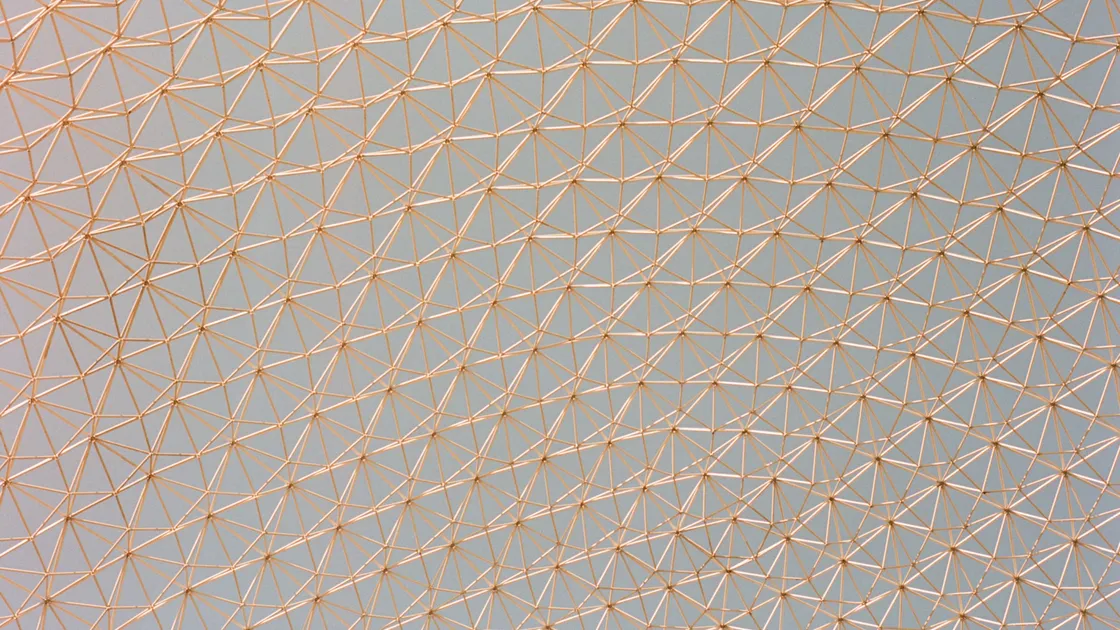 A copper-coloured geodesic lattice of repeated triangular struts seen against a pale sky
